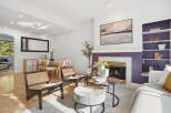 Step into this inviting living space, featuring a cozy fireplace with a striking purple accent wall and a modern abstract painting above.