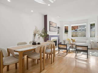 This beautifully staged dining and living area features a modern marble-topped dining table with upholstered chairs, complemented by a cozy living room with a plush white sofa and a stylish fireplace.
