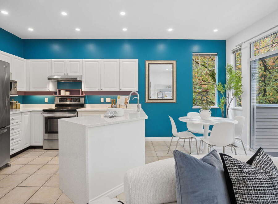 This modern kitchen boasts a striking teal accent wall, complemented by sleek white cabinetry and stainless steel appliances.