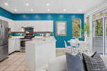 This modern kitchen boasts a striking teal accent wall, complemented by sleek white cabinetry and stainless steel appliances.