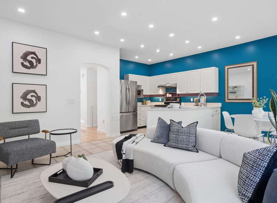 Experience modern living in this open-concept space, featuring a vibrant teal accent wall that beautifully complements the sleek white cabinetry of the kitchen.