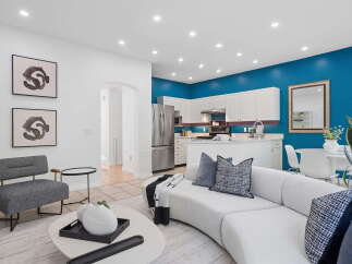 Experience modern living in this open-concept space, featuring a vibrant teal accent wall that beautifully complements the sleek white cabinetry of the kitchen.