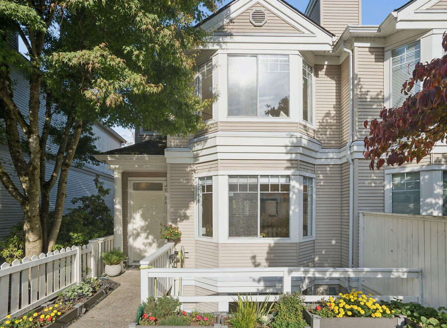 This charming townhouse features a welcoming entrance with a white picket fence and vibrant flower beds.