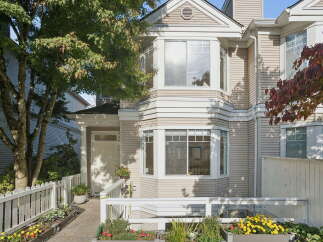 This charming townhouse features a welcoming entrance with a white picket fence and vibrant flower beds.