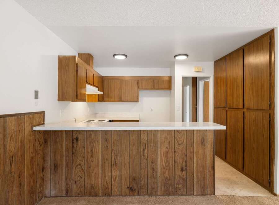 This kitchen features warm wood cabinetry and a breakfast bar with a wood-paneled base, perfect for casual dining.