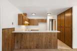 This kitchen features warm wood cabinetry and a breakfast bar with a wood-paneled base, perfect for casual dining.