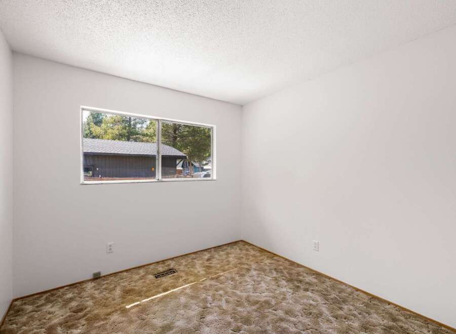 This empty room features a large window offering a view of the surrounding trees and a neighboring house.