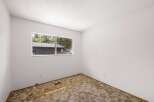 This empty room features a large window offering a view of the surrounding trees and a neighboring house.