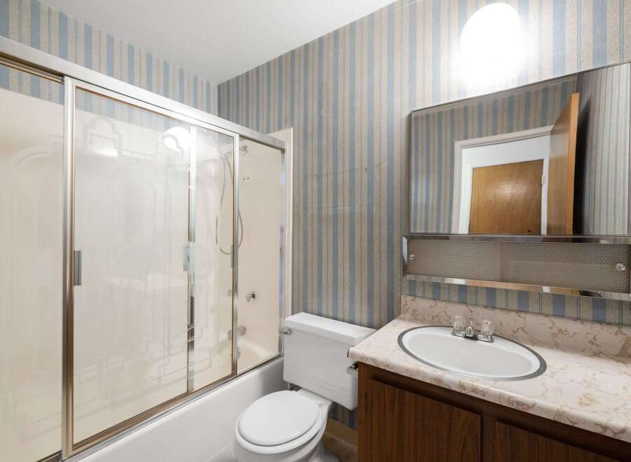 This bathroom features a bathtub with a sliding glass shower door, a white toilet, and a vanity with a marble-patterned countertop.
