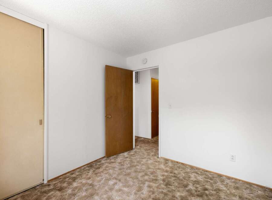This unfurnished bedroom features a large closet with a sliding door and a wooden interior door that opens to a hallway.