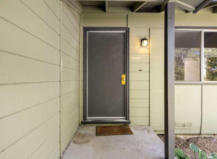 Welcome guests to this charming home with a neutral-toned exterior, featuring a dark gray front door with a brass handle and a welcoming porch light.