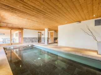 Experience ultimate relaxation in this indoor swimming pool area, featuring a sleek, modern design with a wooden ceiling and stone tile flooring.