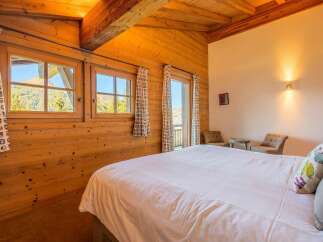 Experience rustic charm in this cozy bedroom, featuring warm, wood-paneled walls and a vaulted ceiling with exposed beams.
