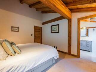 Experience rustic charm and modern comfort in this inviting bedroom, featuring exposed wooden beams and a vaulted ceiling that create a warm, airy ambiance.