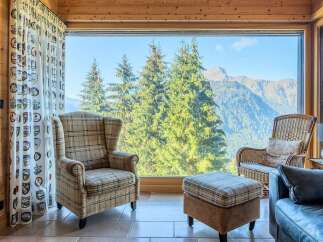 Experience breathtaking mountain views from this cozy living space, featuring a comfortable plaid armchair and ottoman perfect for relaxing.
