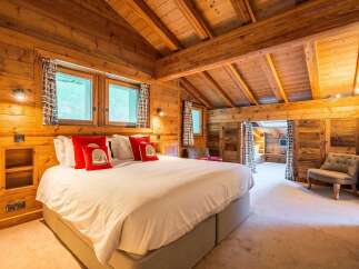 Experience rustic luxury in this charming wooden chalet bedroom, featuring a plush king-sized bed adorned with vibrant red accent pillows.