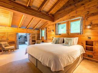 Experience rustic luxury in this charming wooden chalet bedroom, featuring a spacious king-sized bed adorned with plush pillows and a cozy armchair.
