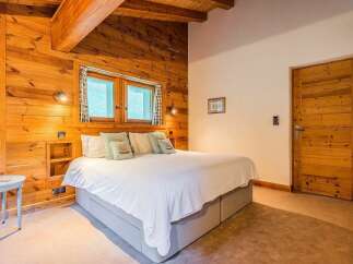 Experience rustic charm in this cozy bedroom featuring warm, wood-paneled walls and exposed wooden beams.