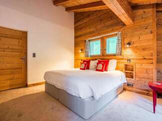 Experience rustic charm in this beautifully appointed bedroom, featuring warm wooden walls and exposed beams that create a cozy alpine ambiance.
