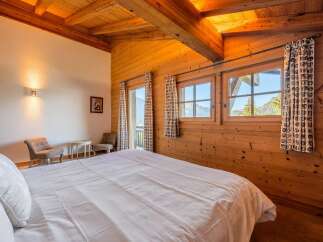 Experience cozy mountain living in this charming bedroom, featuring warm wooden walls and a vaulted ceiling with exposed beams.