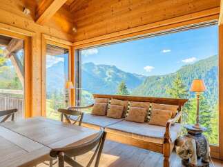 Experience breathtaking mountain views from this stunning living space, featuring a cozy wooden interior and expansive windows.