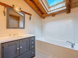 This charming bathroom features a rustic aesthetic with exposed wooden beams and a skylight, bathing the space in natural light.