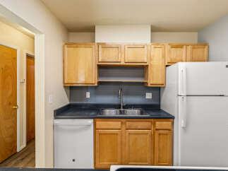 This kitchen features light wood cabinetry offering ample storage space, complemented by a dark countertop and a double basin sink with a modern faucet.