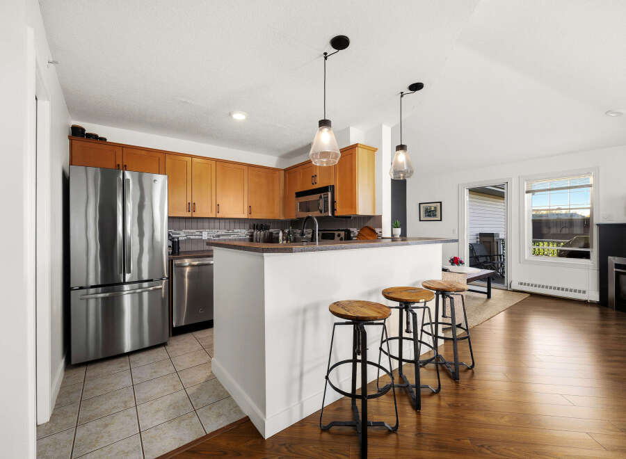 Experience modern living in this beautifully appointed kitchen, featuring sleek stainless steel appliances, warm wood cabinetry, and a convenient breakfast bar with stylish stools.
