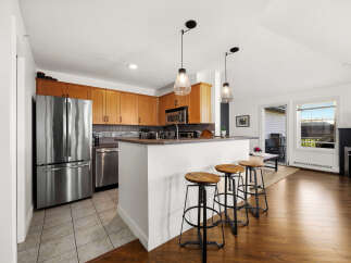 Experience modern living in this beautifully appointed kitchen, featuring sleek stainless steel appliances, warm wood cabinetry, and a convenient breakfast bar with stylish stools.