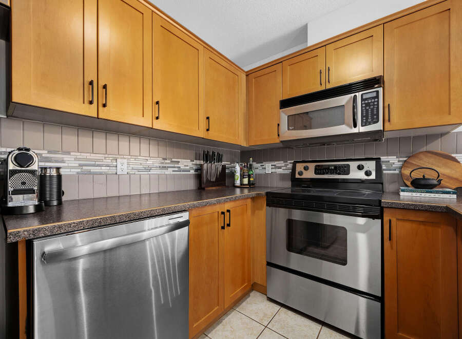 This kitchen boasts modern stainless steel appliances, including a dishwasher, oven, and microwave, complemented by sleek wooden cabinetry.
