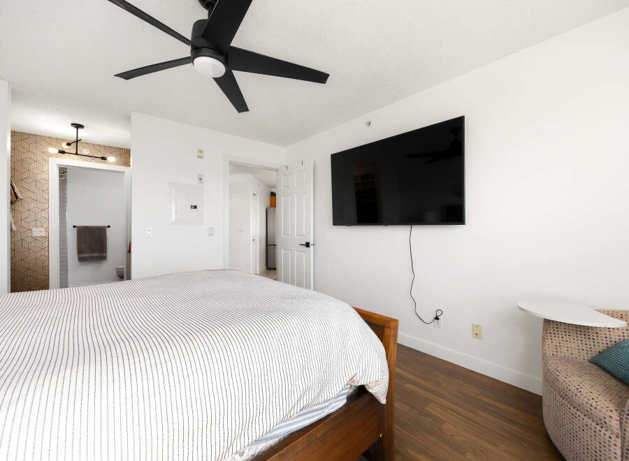 This bedroom offers a comfortable and modern living space, featuring a large flat-screen TV mounted on the wall and a stylish ceiling fan for optimal comfort.