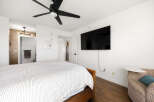 This bedroom offers a comfortable and modern living space, featuring a large flat-screen TV mounted on the wall and a stylish ceiling fan for optimal comfort.