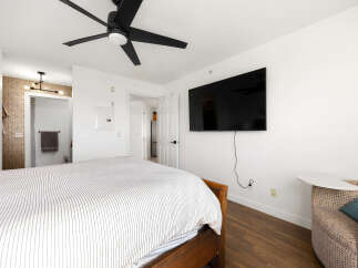 This bedroom offers a comfortable and modern living space, featuring a large flat-screen TV mounted on the wall and a stylish ceiling fan for optimal comfort.