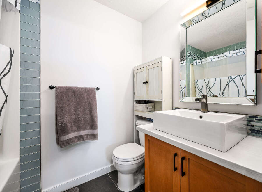 This modern bathroom features a sleek white vessel sink atop a warm wood vanity, complemented by a large, ornate mirror.