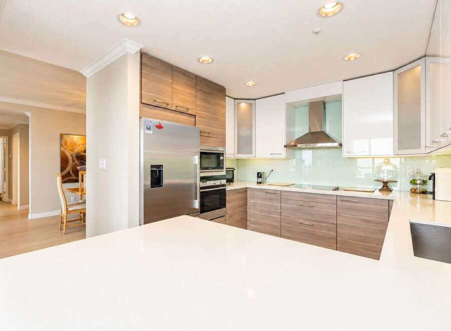 Experience modern living in this stunning kitchen featuring sleek white and wood-grain cabinetry, complemented by a stylish stainless steel range hood and a light blue glass backsplash.