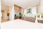 Experience modern living in this stunning kitchen featuring sleek white and wood-grain cabinetry, complemented by a stylish stainless steel range hood and a light blue glass backsplash.