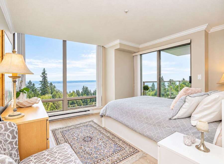 Experience breathtaking panoramic views from this stunning bedroom, featuring floor-to-ceiling windows that showcase the serene water and lush greenery.