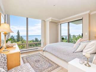 Experience breathtaking panoramic views from this stunning bedroom, featuring floor-to-ceiling windows that showcase the serene water and lush greenery.