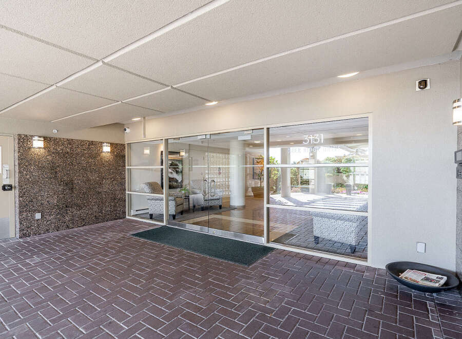 Welcome to this inviting building entrance, featuring a modern glass facade and a well-maintained brick walkway.