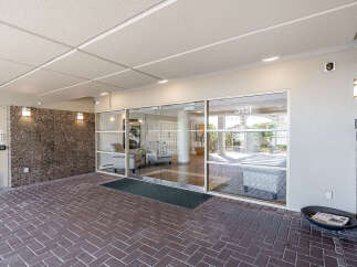 Welcome to this inviting building entrance, featuring a modern glass facade and a well-maintained brick walkway.