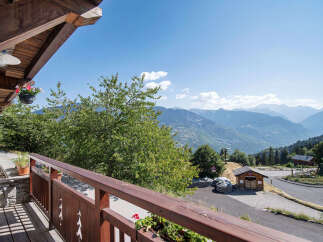 Enjoy breathtaking mountain views from this charming property's balcony, complete with a hanging flower basket and wooden railing.
