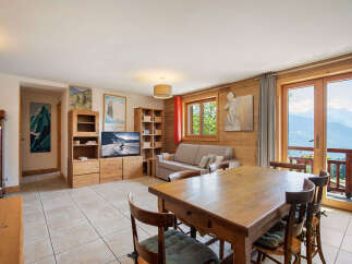 Experience breathtaking mountain views from this charming living and dining area, featuring a cozy sofa, a large wooden dining table, and a modern entertainment center.