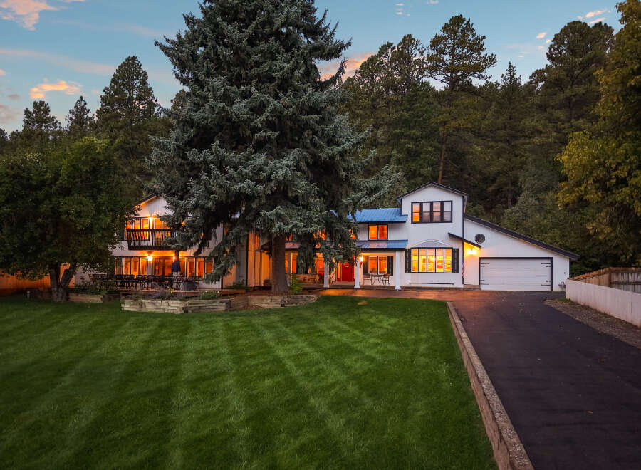 Nestled amidst a lush forest, this stunning white home boasts a striking blue metal roof and multiple levels of balconies perfect for enjoying the serene surroundings.