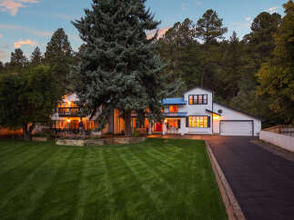 Nestled amidst a lush forest, this stunning white home boasts a striking blue metal roof and multiple levels of balconies perfect for enjoying the serene surroundings.