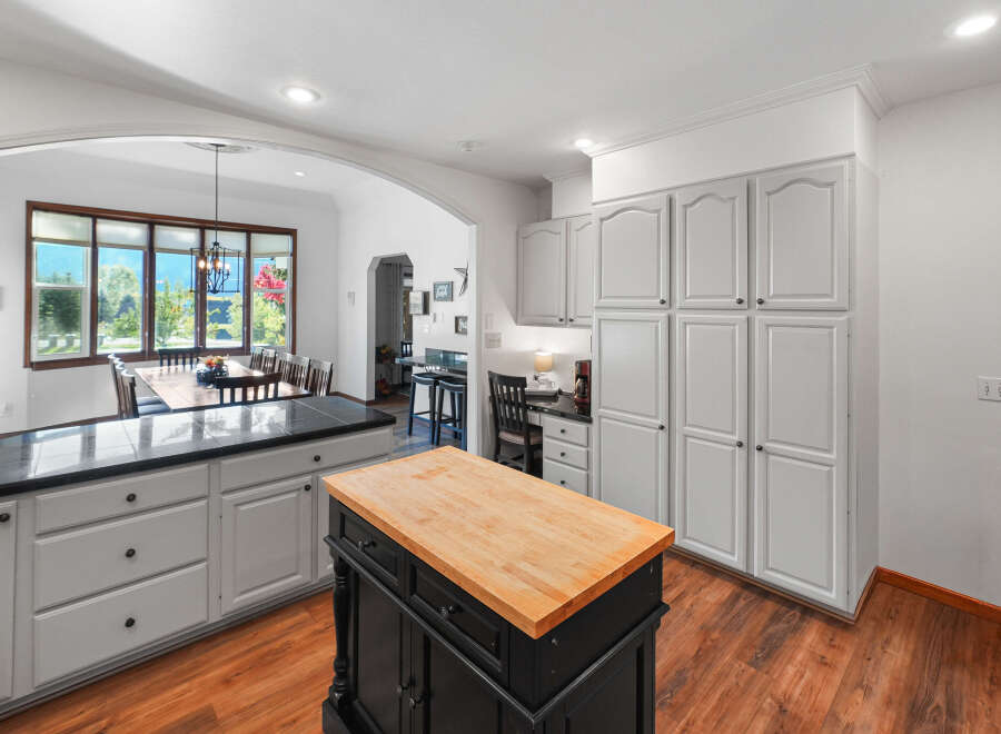 This spacious kitchen boasts ample storage with a wall of white cabinets and a large island featuring a butcher block countertop.