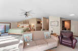 This spacious loft bedroom offers a comfortable king-size bed with a light green quilt and decorative pillows, complemented by a cozy seating area featuring a beige sofa and a rich brown leather armchair.