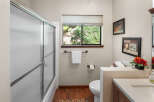 This bathroom offers a refreshing retreat with a frosted glass shower door and a large window overlooking lush greenery.