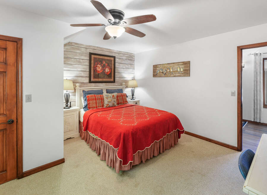 This charming bedroom features a cozy queen-size bed adorned with a vibrant red quilt and plaid accents, set against a rustic wood-plank accent wall.