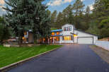 Nestled amidst towering pine trees, this stunning modern farmhouse boasts a crisp white exterior with black trim and a striking blue metal roof.