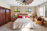 Experience rustic charm in this inviting bedroom featuring a grand wooden barn door and a striking windmill-inspired ceiling fan.